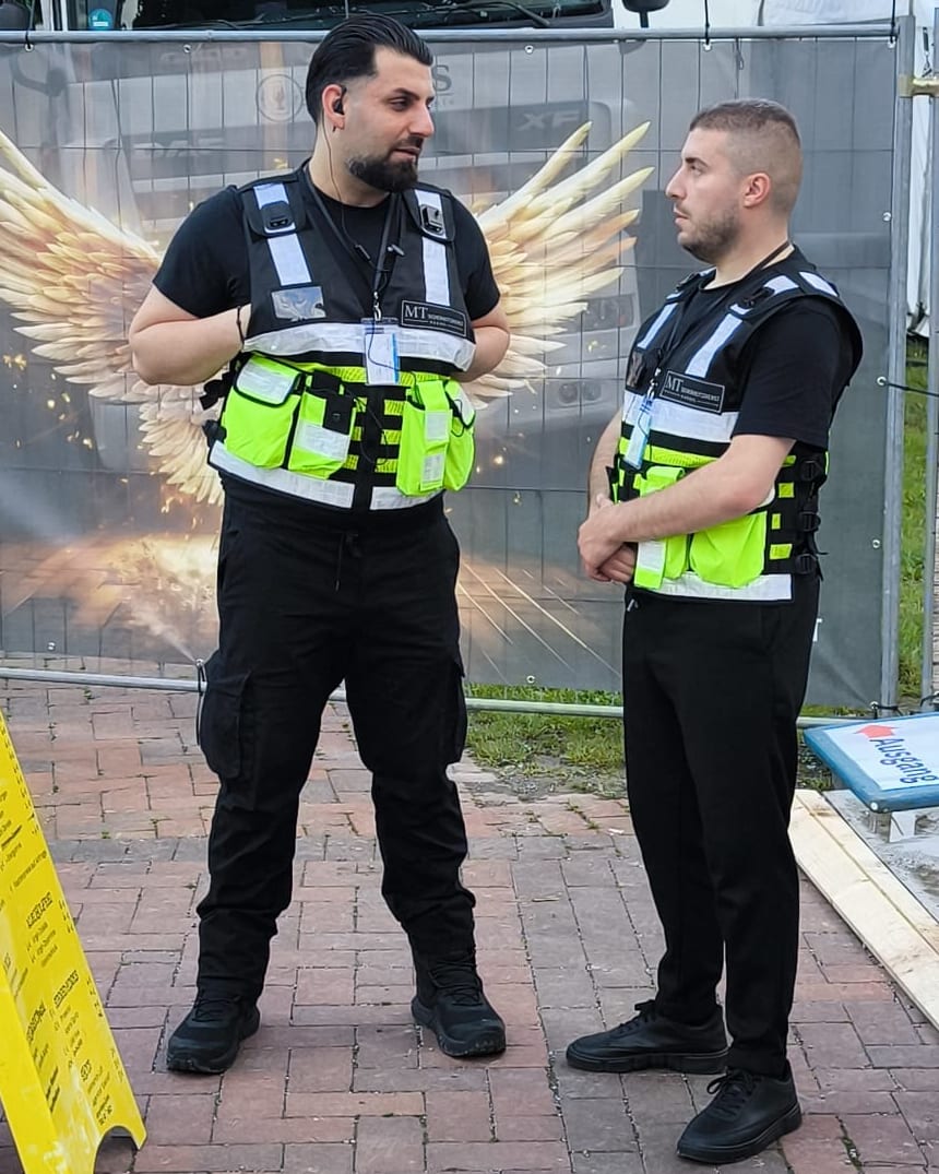 Zwei Mitarbeiter des MT-Ordnungsdiensts in Warnwesten bei der Absprache auf einem Veranstaltungsgelände